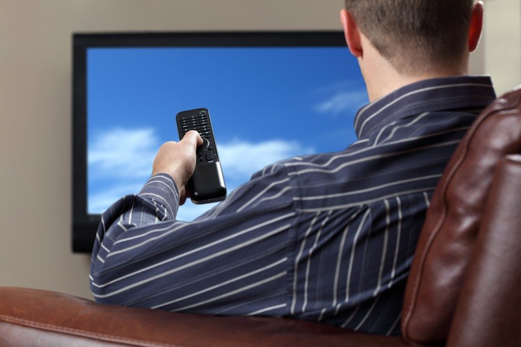 Man sitting on a sofa watching TV and holding a remote