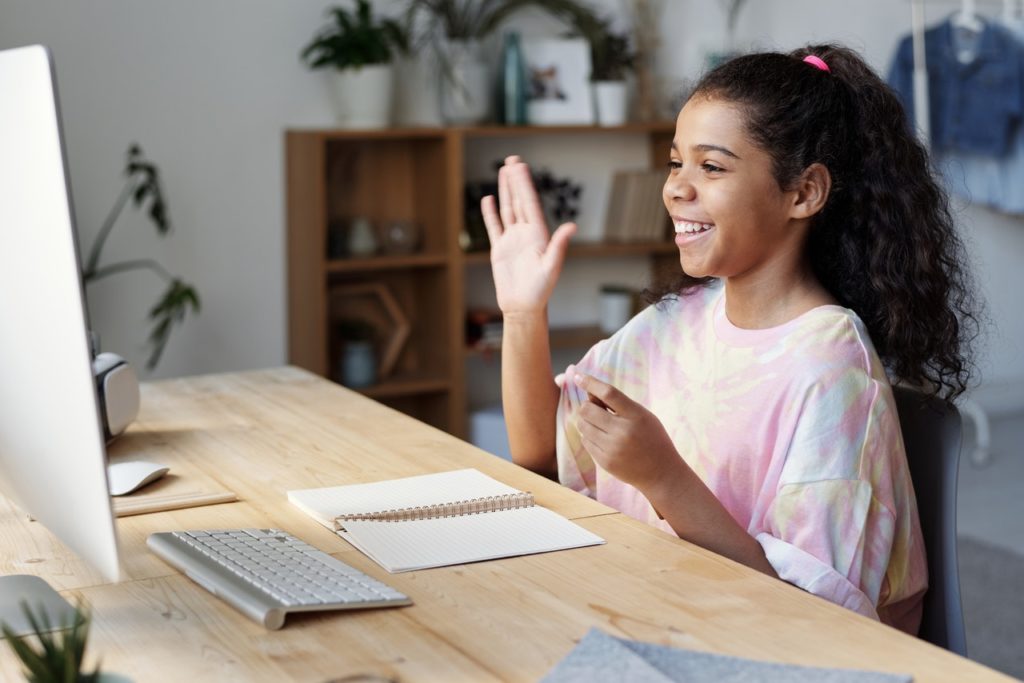 young girl raising hand reciting during an online class