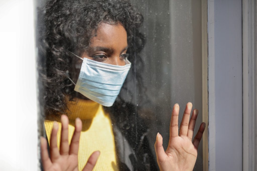 woman wearing facemask looking outside window
