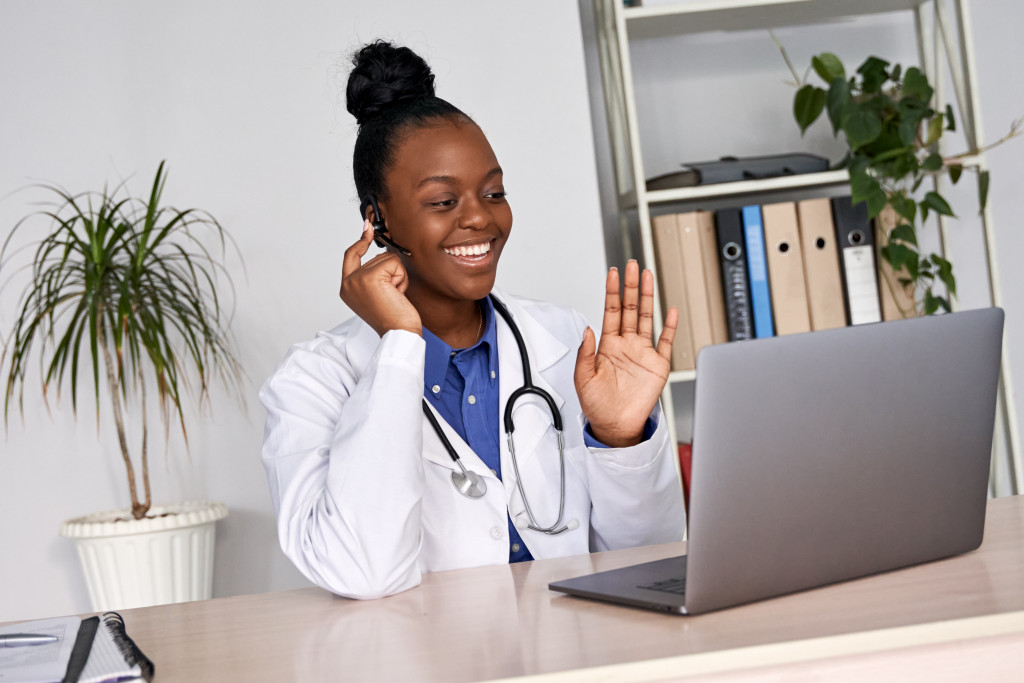 female doctor smiling and waving at patient in the laptop during telemedicine session