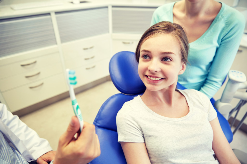 a dentist showing proper toothbrush techniques to a teen