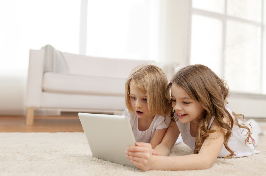 two little girls with tablet pc computer lying on floor at home